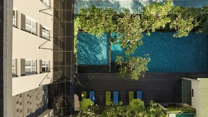 A rooftop pool with a tiled wall, surrounded by greenery and a building with multiple windows.