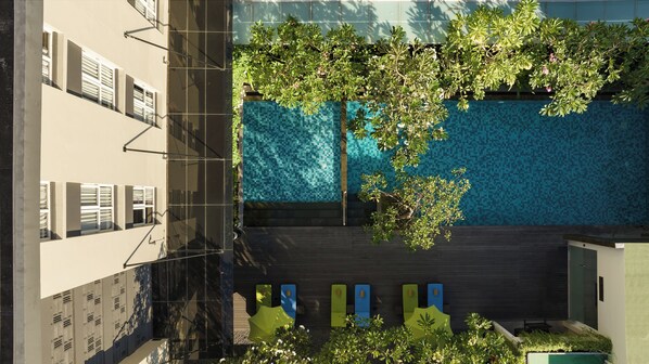 A rooftop pool with a tiled wall, surrounded by greenery and a building with multiple windows.