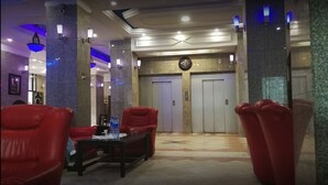 A lobby with red chairs, a table, and two elevators. - Grand Hotel Adghir (Algiers)