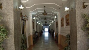 A long, well-lit hallway with a tiled floor, flanked by columns and potted plants, leading to a large open space. - Grand Hotel Adghir (Algiers)