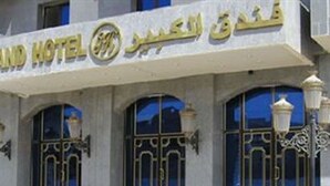 A hotel facade with a sign in Arabic and English, large arched windows, and decorative ironwork. - Grand Hotel Adghir (Algiers)