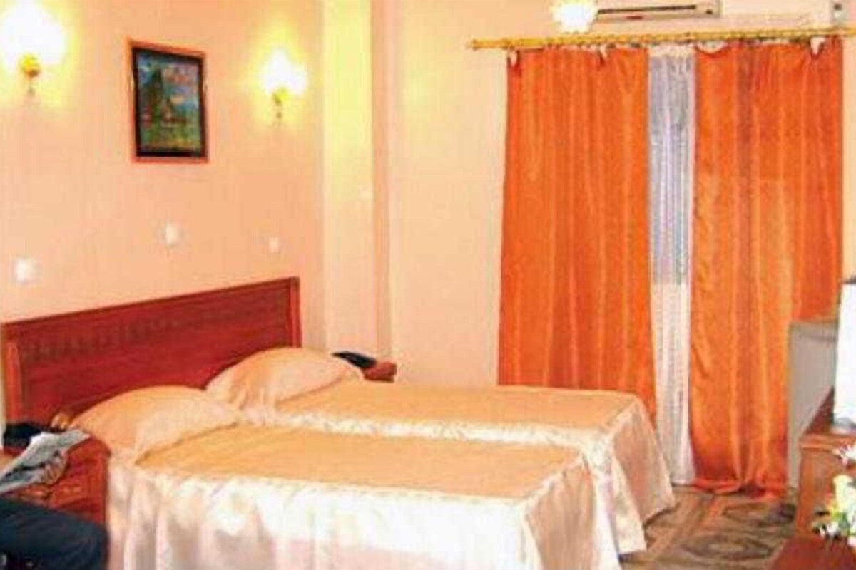 Une chambre d’hôtel avec deux lits, une tête de lit en bois, une petite table et un rideau.