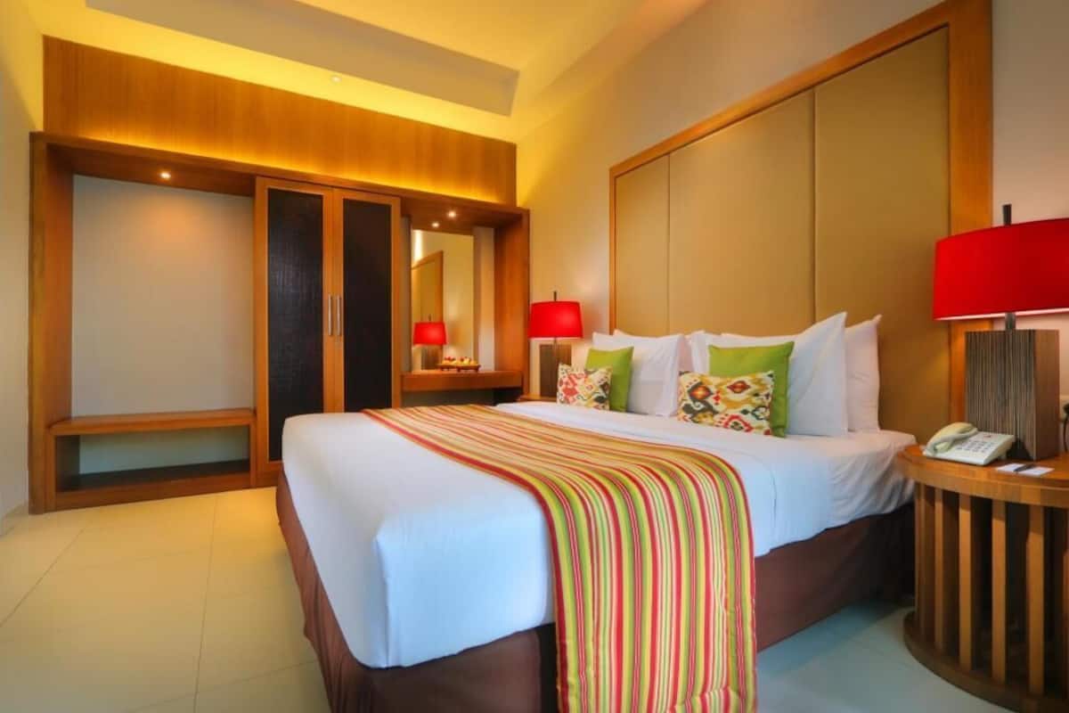 A hotel room with a large bed, wooden headboard, bedside tables with lamps, and a mirror.