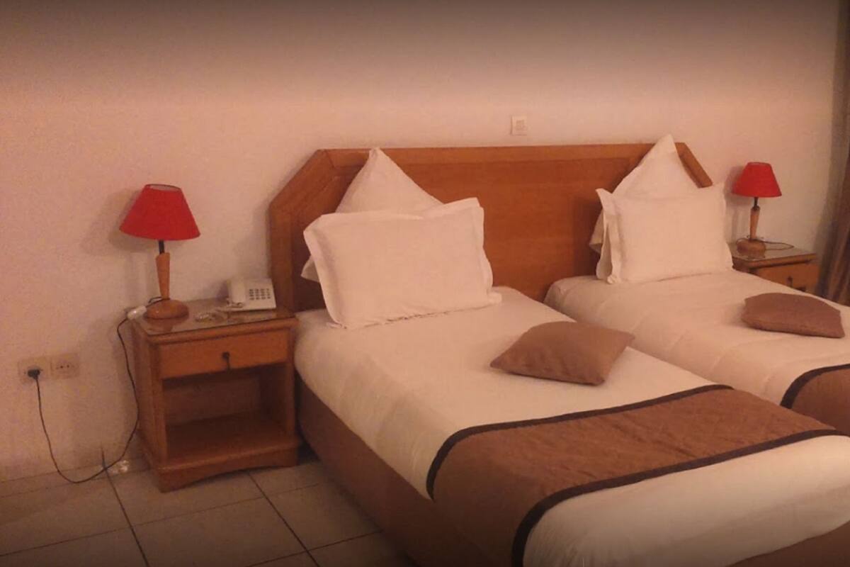 A double bed with white and brown bedding, two bedside tables with lamps, and a window with curtains.