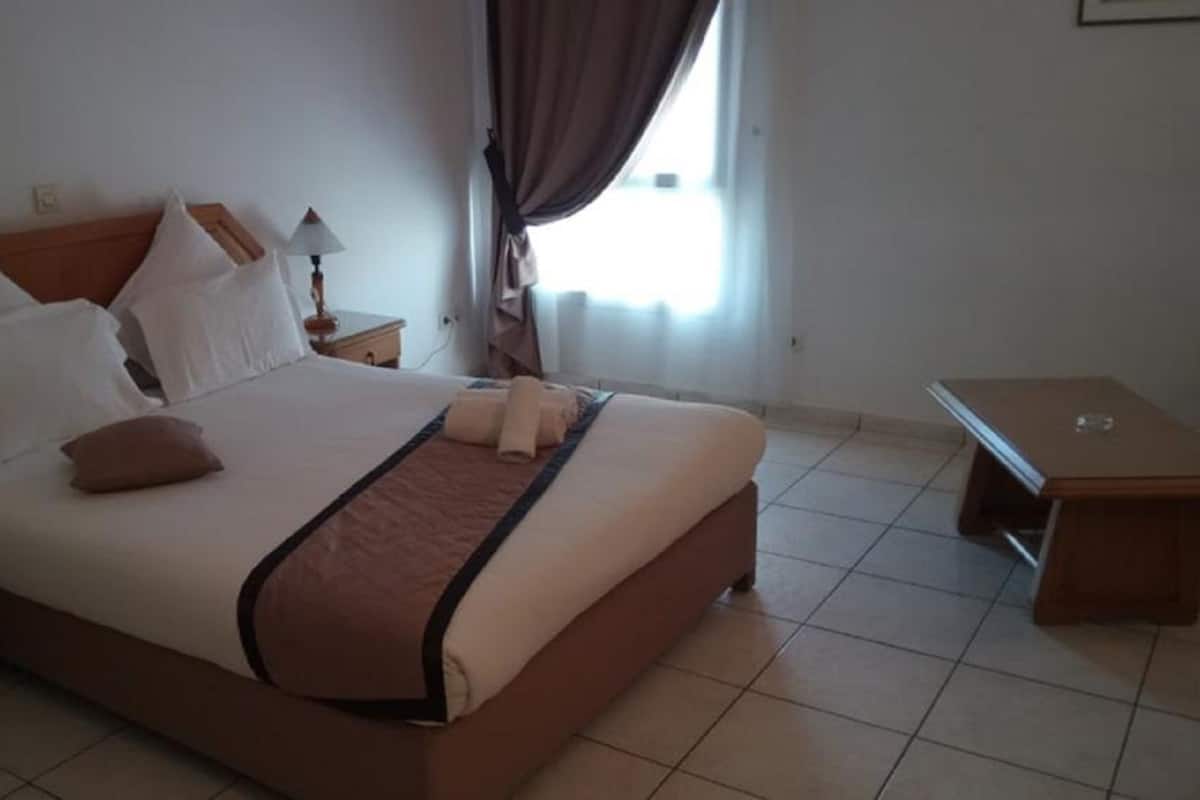 A hotel room with a large bed, a nightstand, a desk, and a window with curtains.