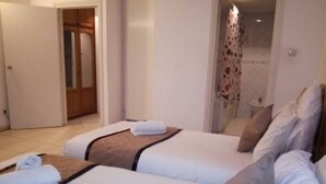 A hotel room with two beds, a bathroom with a shower curtain, and a door leading to another room. - El Biar Hotel (Algiers)