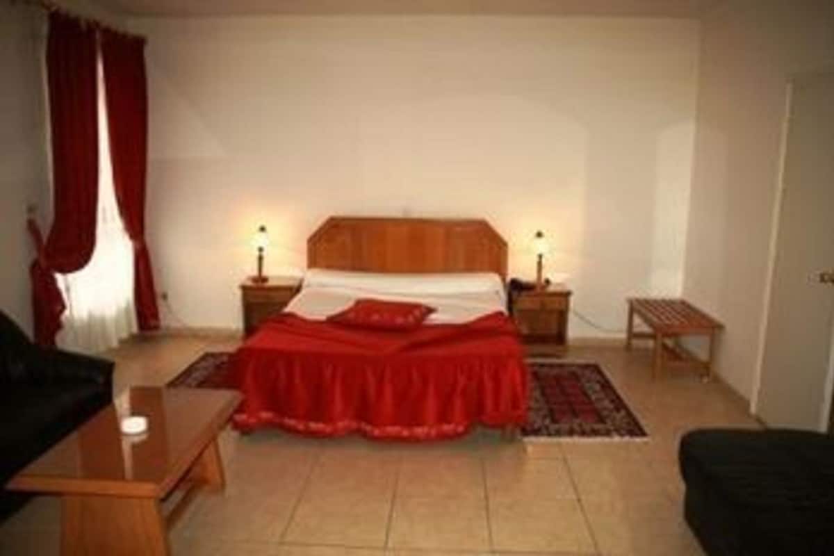 A bedroom with a bed, two bedside tables, a nightstand, a small table, and a chair.