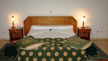 Un dormitorio con cabecera de madera, colcha estampada verde, dos lámparas de noche y una mesita de noche con un teléfono.