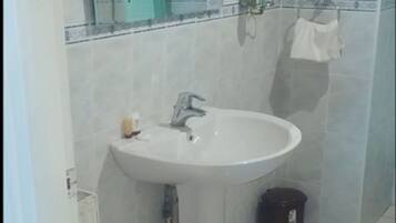 A bathroom with a white sink, a mirror, and a trash bin.