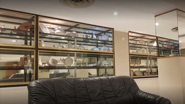 A room with a black leather sofa, a glass display case with various ceramic items, and a white cabinet. - El Biar Hotel (Algiers)