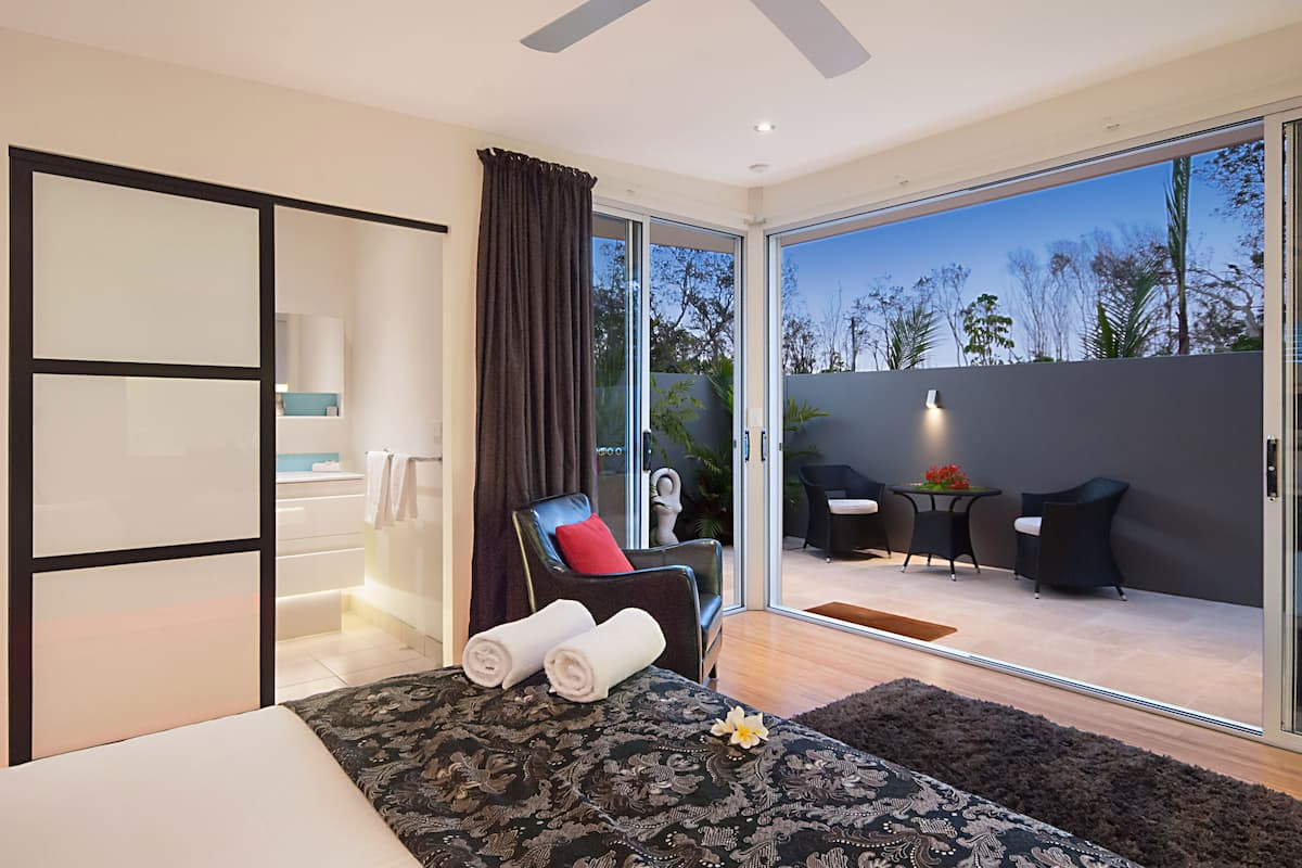 Habitación de hotel moderna con cama, sillón de masaje, una mesita con sillas y vistas al exterior.