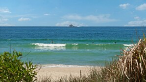 A beach with clear blue water, waves, and a distant island. - Cavvanbah (Byron Bay)