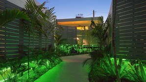 A pathway flanked by green plants and a modern building with horizontal slats. - Cavvanbah (Byron Bay)