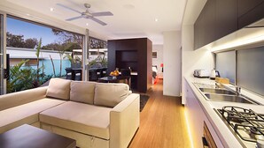 A modern kitchen with a gas stove, a dining area with a table and chairs, and a large window overlooking a garden. - Cavvanbah (Byron Bay)
