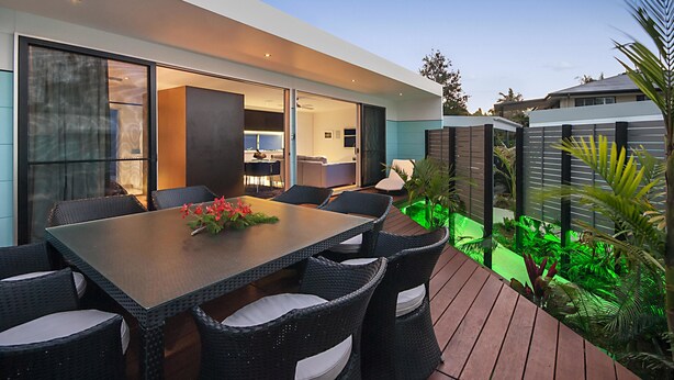 A modern outdoor dining area with a large table and chairs, surrounded by greenery and a wooden deck. - Cavvanbah (Byron Bay)