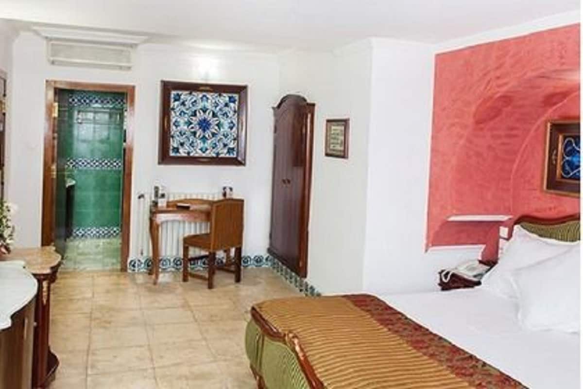 A hotel room with a bed, a desk with a chair, a television, a bathroom with a sink and mirror, and a door leading to another room.