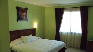 A hotel room with a single bed, a nightstand, a painting on the wall, and a window with curtains. - Hotel Sweet (Algiers)