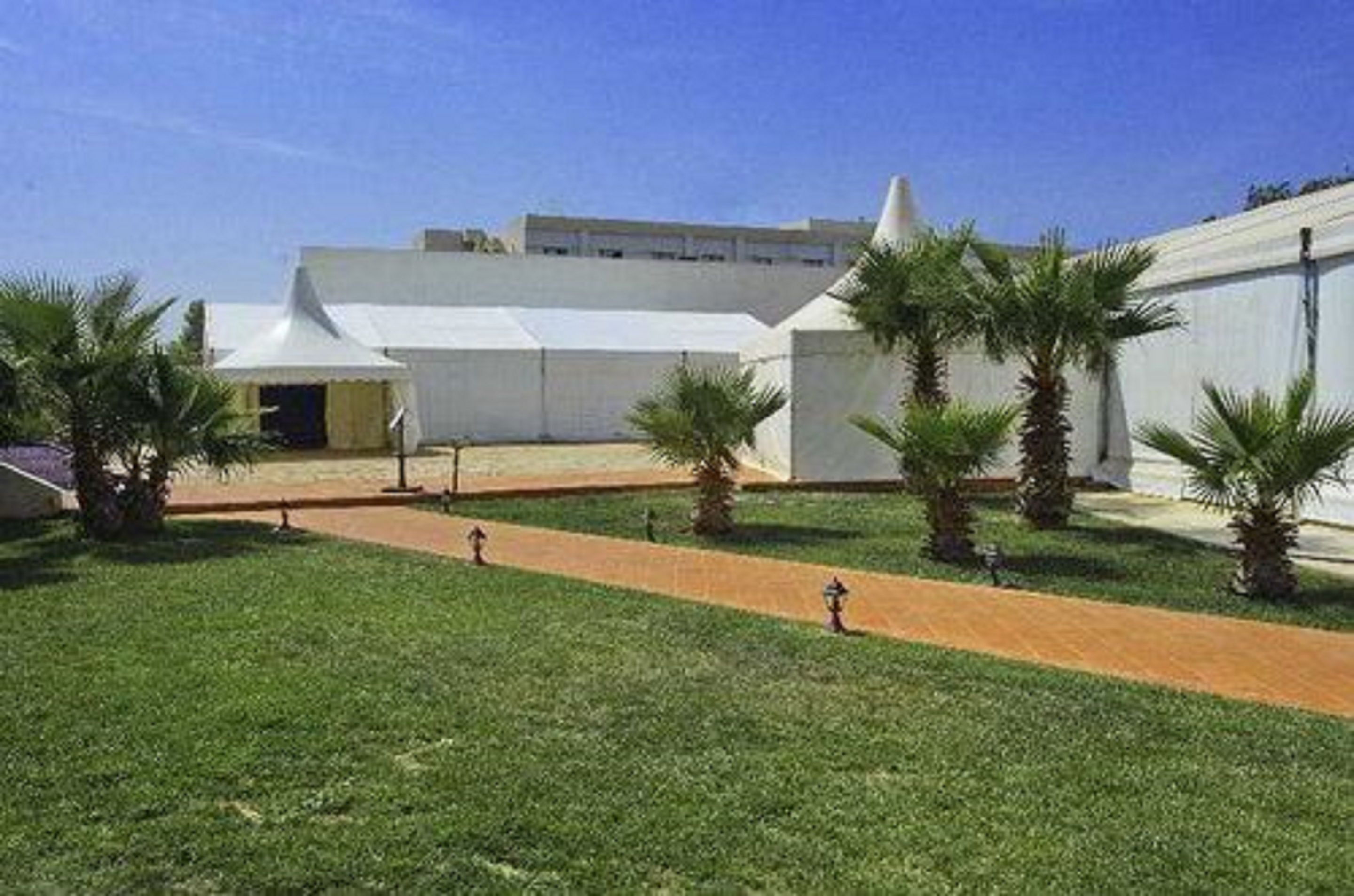 A modern building with a flat roof, surrounded by a well-maintained lawn and palm trees.