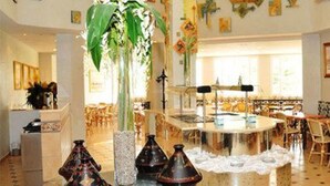 A spacious dining area with round tables and chairs, a central decorative piece, and a large plant. - Eden Phoenix (El Kerma)
