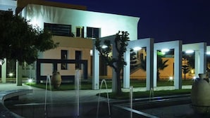 A modern building with a fountain in the foreground, large decorative vases, and a well-lit entrance. - Eden Phoenix (El Kerma)