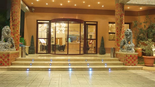 A hotel entrance with a revolving door, steps leading up to it, and two lion statues on either side. - Eden Phoenix (El Kerma)