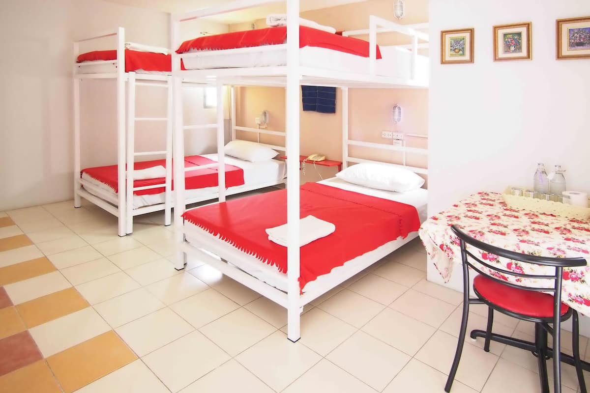 Quarto com beliches, uma pequena mesa com cadeiras e um telefone fixado na parede.