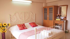 A neatly made bed with two pillows, a bedside table with a mirror, and a wooden wardrobe.