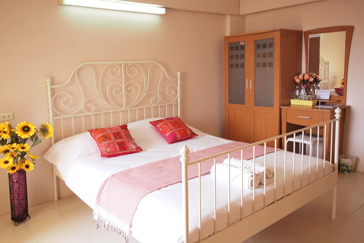 Cama bem arrumada com duas almofadas, mesa de cabeceira com espelho e guarda-roupa de madeira.