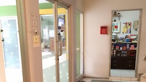 A hallway with a checkered floor, a glass door with a handle, and a small red mailbox on the wall.