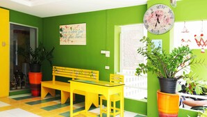A brightly colored room with a yellow bench, a clock, and various plants.