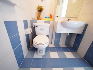 A bathroom with a white toilet, a sink, and blue and white tiled floors. - Thanapa Mansion - Hostel (Bangkok)