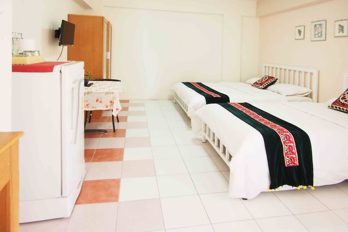 Quarto de hotel com duas camas, uma escrivaninha, um frigorífico e uma televisão presa à parede.