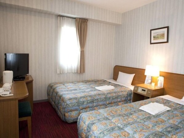 Habitación de hotel con dos camas, televisión, escritorio con teléfono y ventana con cortinas.