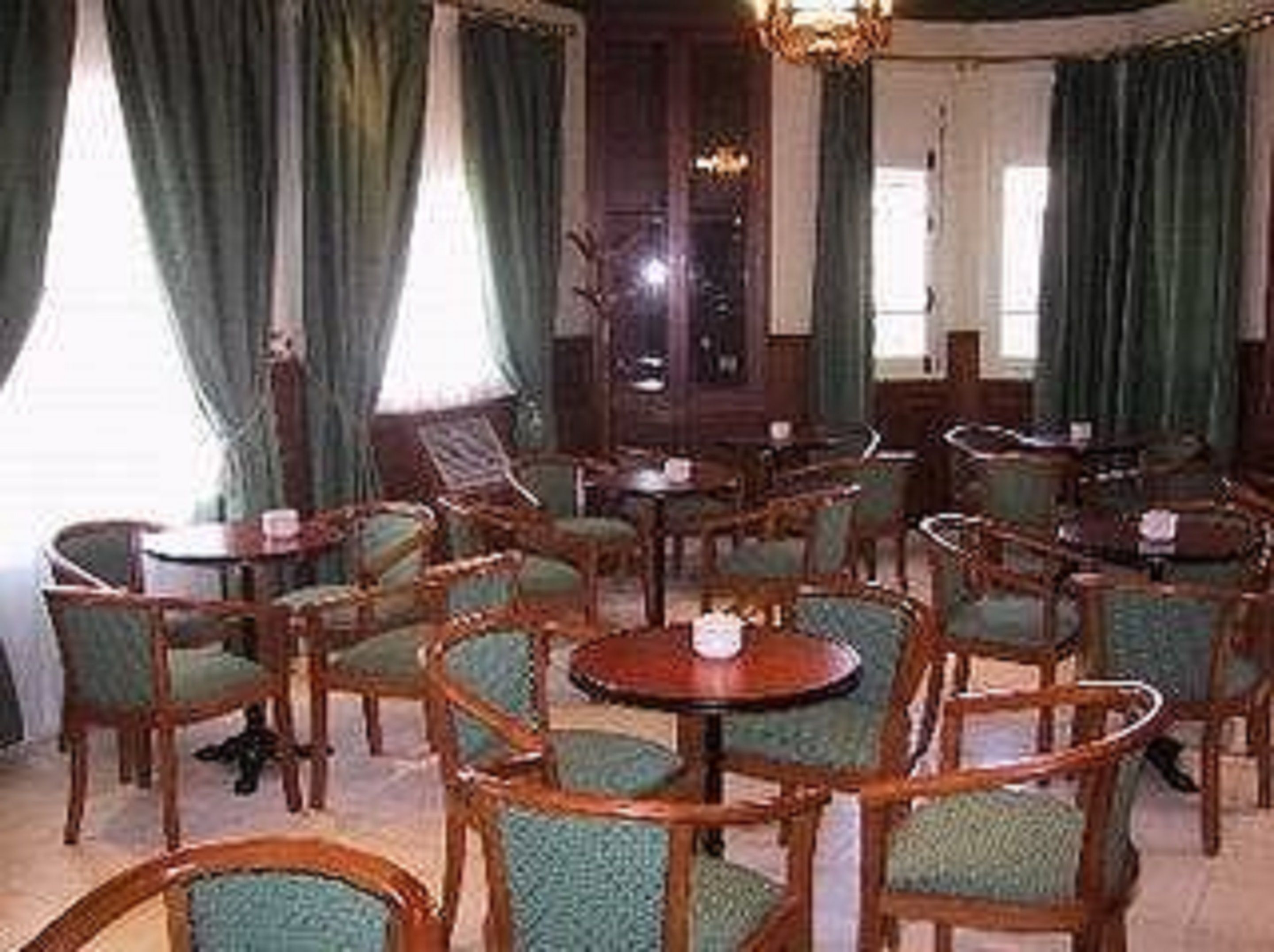 Une pièce dotée de plusieurs tables en bois et de chaises recouvertes d’un tissu vert, disposées dans un coin repas accueillant et bien éclairé.