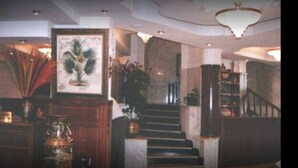 Un magnifique escalier en marbre, orné d’un lustre, mène à un palier où est accrochée une grande estampe botanique encadrée.