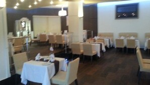 Un espace repas avec des tables dressées pour accueillir plusieurs convives, chacune étant recouverte d’une nappe blanche et agrémentée d’un présentoir à menus.