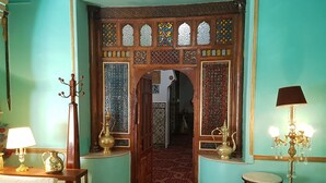 A room with a patterned carpet, a wooden door with intricate designs, a white sofa, and a small table with a vase. - Hotel El-Djazair (Algiers)