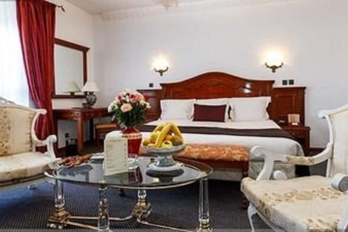 A hotel room with a large bed, two armchairs, a small table with a vase of flowers, and a nightstand with a lamp.