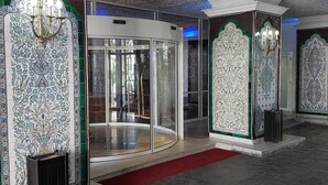 A lobby with ornate tile walls, a revolving door, and a red carpet. - Hotel El-Djazair (Algiers)
