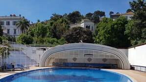 A swimming pool with a curved glass enclosure, surrounded by a wooden deck and lounge chairs. - Hotel El-Djazair (Algiers)