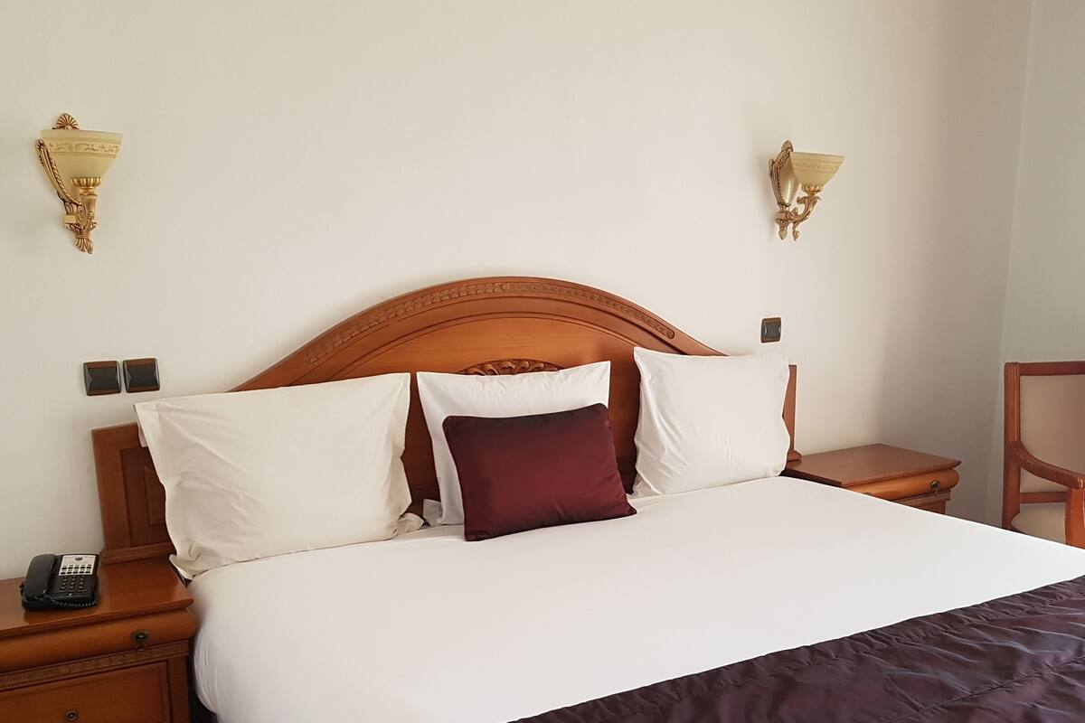A neatly made bed with white and maroon bedding, a wooden headboard, and two bedside tables with lamps.