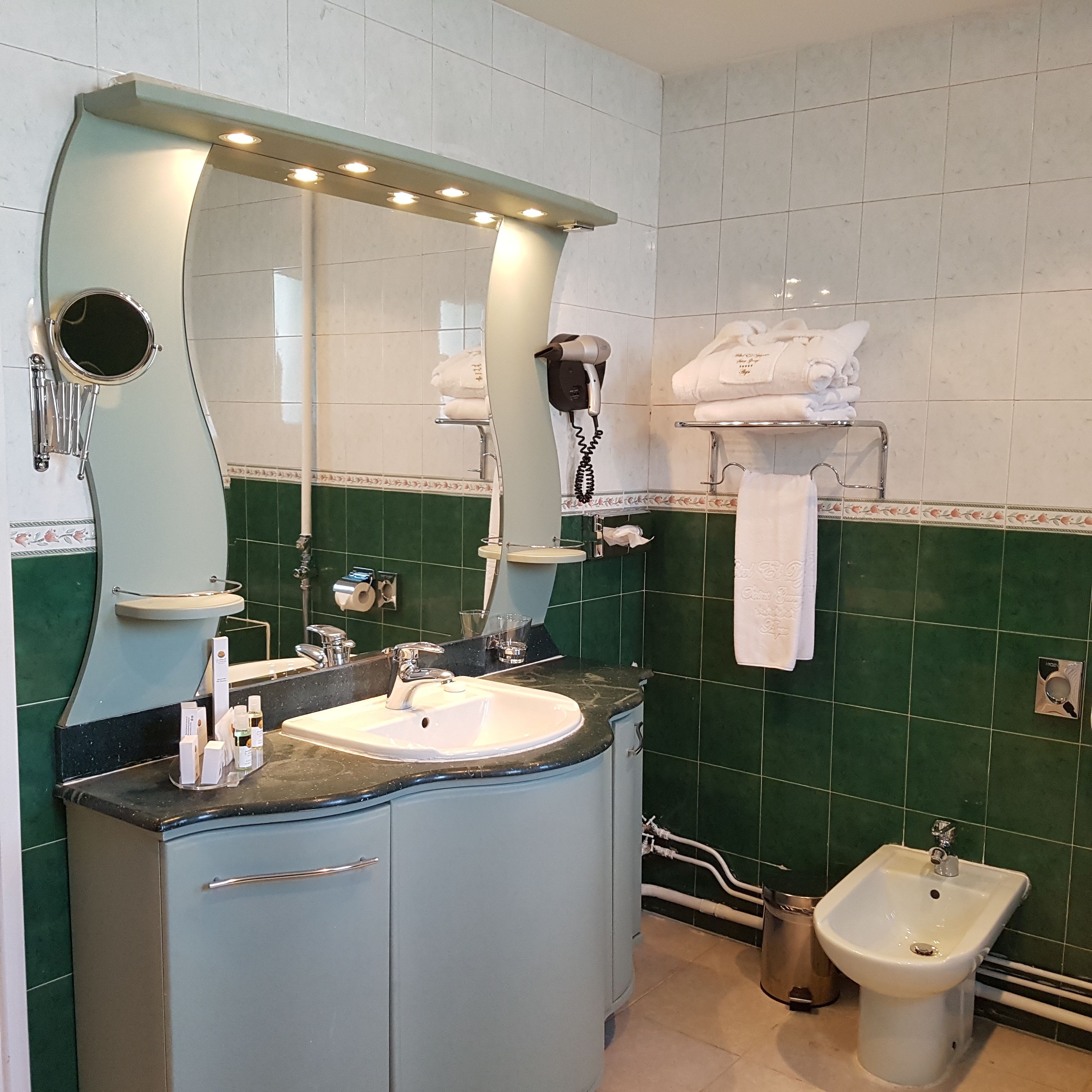 Un baño con un espejo grande, dos lavamanos, un bidé y toalleros.