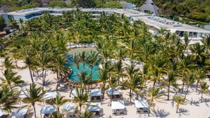 Vista aérea de un resort con piscina central rodeada de palmeras y sillas de playa.
