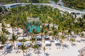 Vista aérea de un resort con piscina central rodeada de palmeras y sillas de playa.