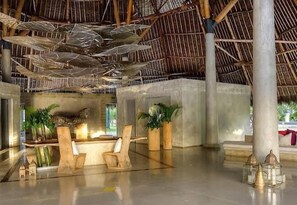 A spacious lobby with a high ceiling, concrete pillars, and a thatched roof. There are wooden chairs and potted plants. - Billionaire Resort & Retreat (Malindi)