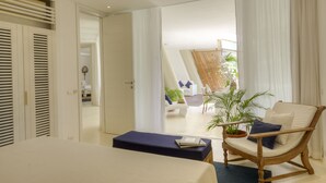 Un dormitorio con una cama, una silla de madera, una mesita y vistas a un balcón con planta y una silla blanca.