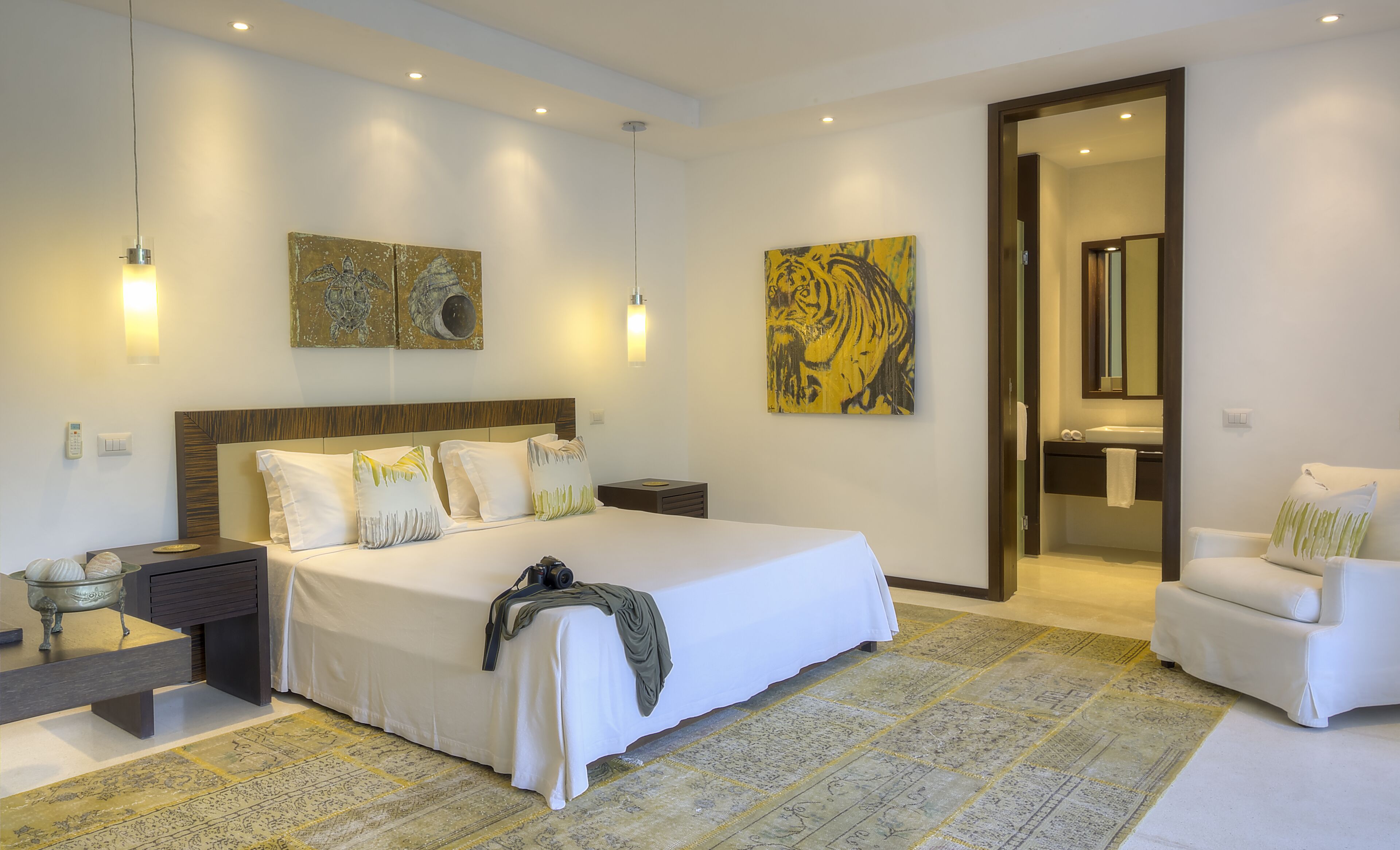 A modern bedroom with a large bed, bedside tables, a chair, and artwork on the walls.