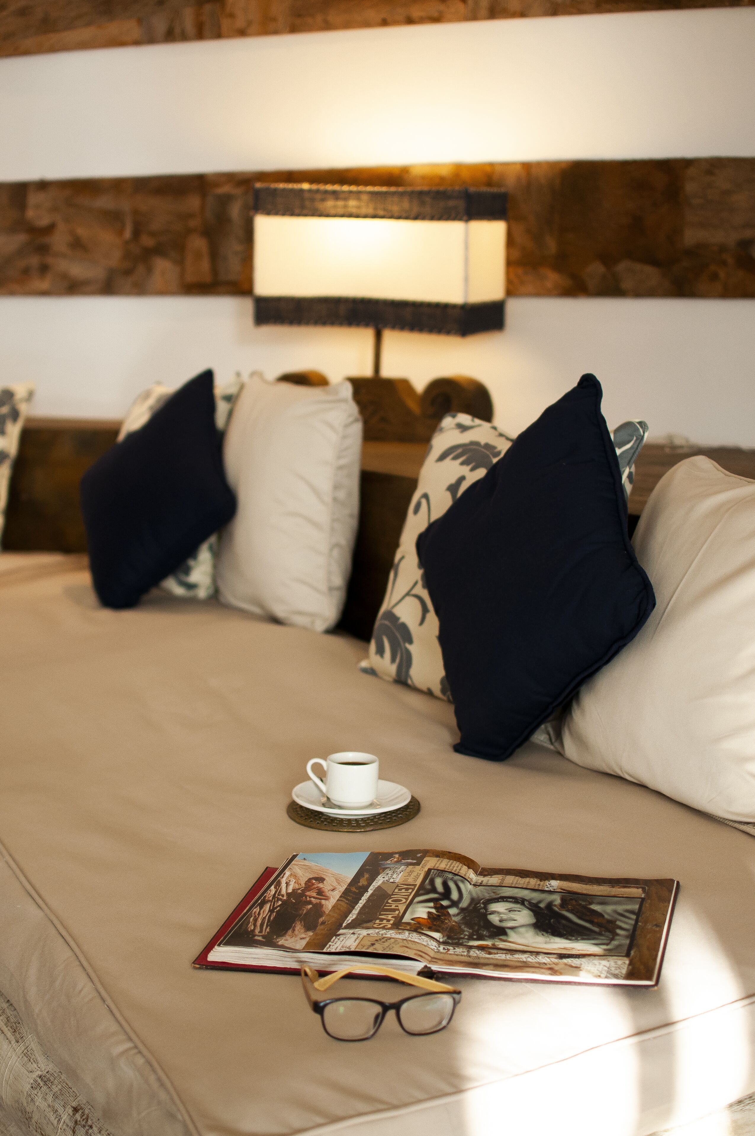 Ein ordentlich bezogenes Bett mit Lampe, Kissen, Tasse und Buch.