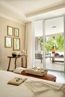 A hotel room with a bed, a bedside table with a tray of items, a window with a view of the outdoors, and a door leading to a balcony.