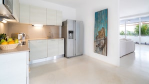 Una cocina moderna con armarios blancos, un refrigerador de acero inoxidable y un amplio ventanal con vistas al exterior.